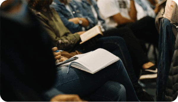 A row of people sitting down at a church with notebooks and bibles in their laps.